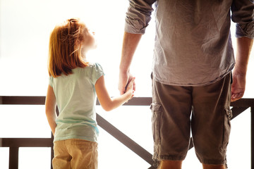 A young girl holds hands with an adult, both standing side by side and facing a bright, sunlit background. The warm scene suggests a close and caring relationship, reflecting the nurturing bond often found in sole custody Tennessee families.