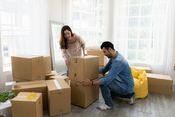 A woman and a man are surrounded by cardboard boxes in a bright room with large windows, unpacking after moving into a new home—perhaps starting fresh together with a cohabitation agreement.