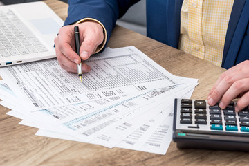 A person in business attire fills out tax forms at a desk, using a pen, calculator, and laptop, while reviewing whether child support is taxable.