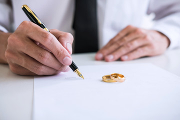 man signing divorce papers with wedding bands