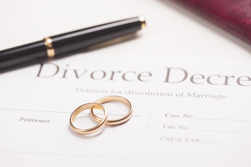 Two gold wedding rings rest on top of a divorce decree document, with a black pen nearby, symbolizing when divorce finalized and the end of a marriage.