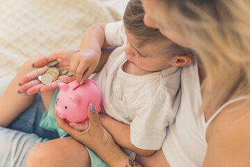 A woman holds a toddler and a pink piggy bank while the child puts coins inside, teaching about saving money and the importance of child support mandatory for financial security.
