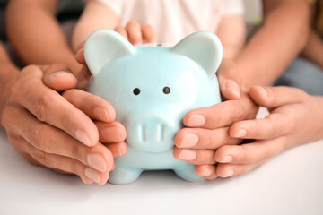 Several hands of adults and a child gently hold a light blue piggy bank together, symbolizing saving money as a family, financial security, and planning for when child support ends at 18.