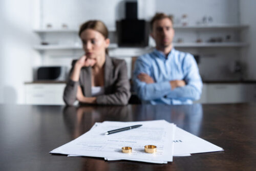 woman and man with arms crossed and divorce papers with rings