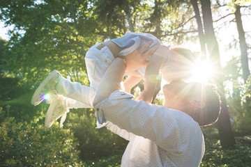 A parent lifts a young child into the air outdoors, both smiling joyfully. Sunlight streams through the trees, creating a warm, bright atmosphere in the green park—moments like these show why it’s difficult to get sole custody.