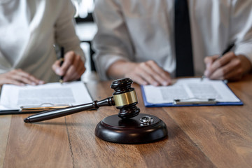 A judge's gavel rests on a wooden table, with two people in business attire sitting behind it, reviewing separation agreements required on their clipboards.