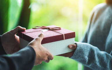 Two people are seen exchanging a gift wrapped in a red and white box with a ribbon, symbolizing how we keep gifts to cherish special moments, whether in marriage or after divorce, against a blurred green and yellow background.