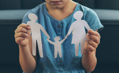 A child in a blue dress holds paper cutouts of a family—two adults and one child—symbolizing family and togetherness, even as custody arrangements changed after divorce. The child’s face is partially visible.