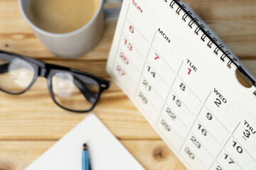 A desk with a calendar marking the first days of the month—reminding of a waiting period for divorce—a pair of black eyeglasses, coffee, and a pen on a white notepad, all neatly arranged on a wooden surface.