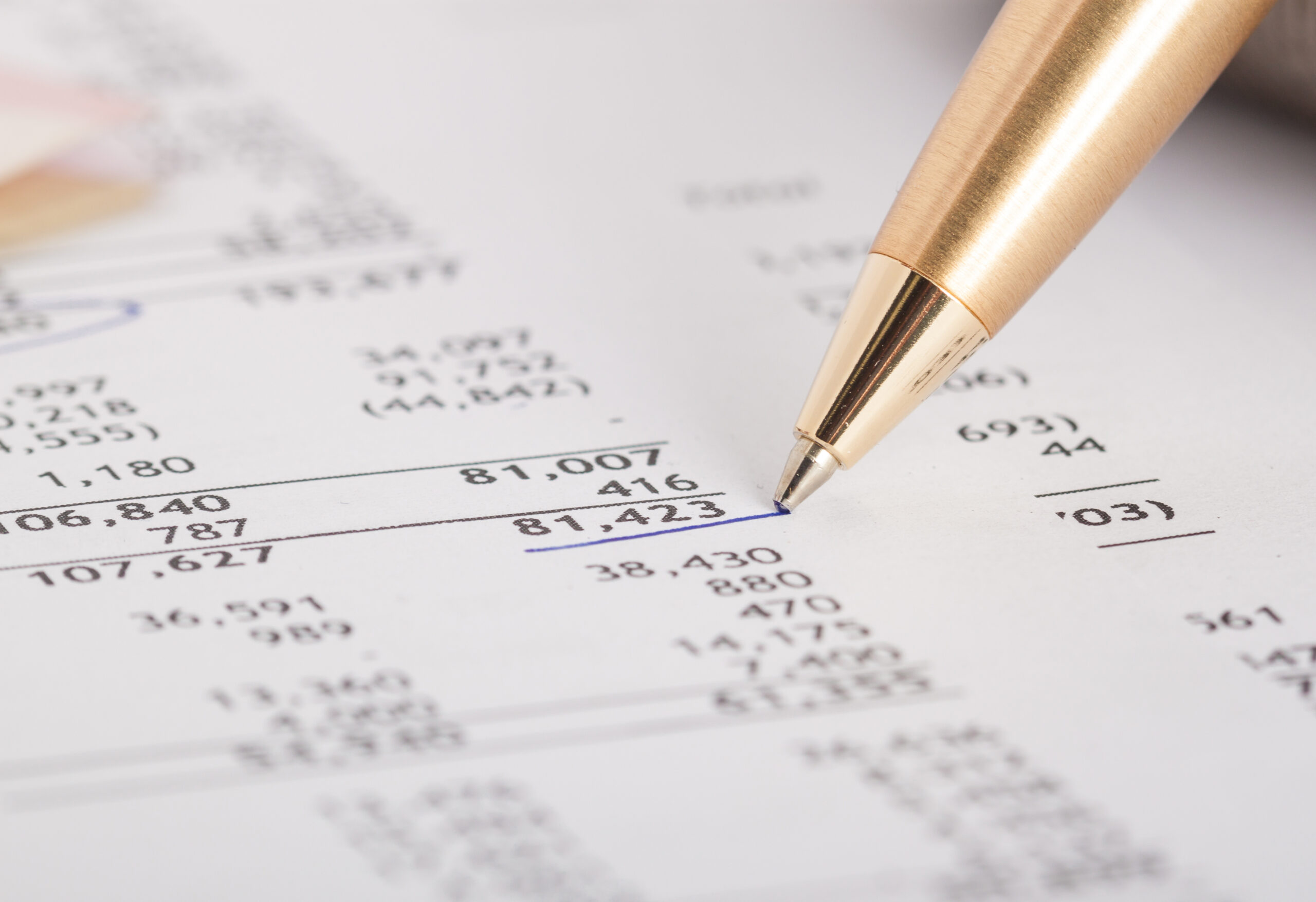 A close-up of a gold pen pointing at financial data on a printed spreadsheet highlights the crucial role of financial disclosure in the divorce process, with rows of numbers and 81,423 underlined in blue.