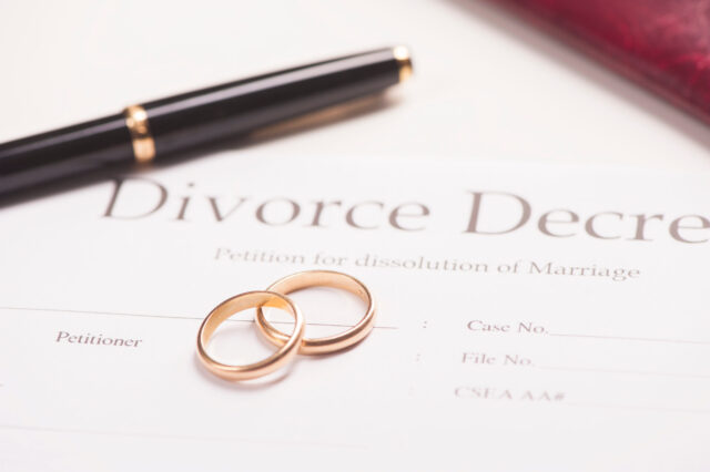 A divorce decree form with two gold wedding rings placed on it, alongside a black pen and part of a red leather folder in the background.